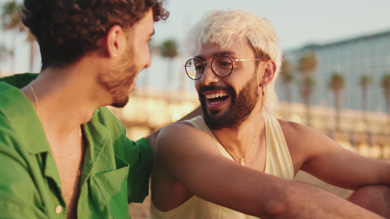 Felice giovane coppia gay che parla e sorride sulla spiaggia