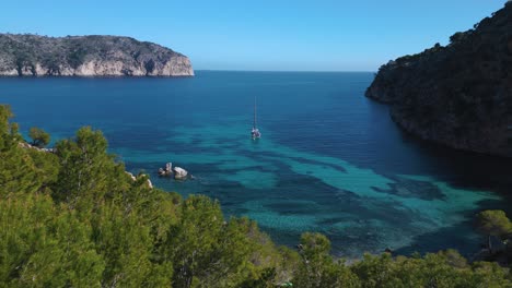 Palma-de-Mallorca-Island,-pristine-beach-bay-clear-turquoise-water-with-trees-and-yacht-ship-sailing-boat-at-on