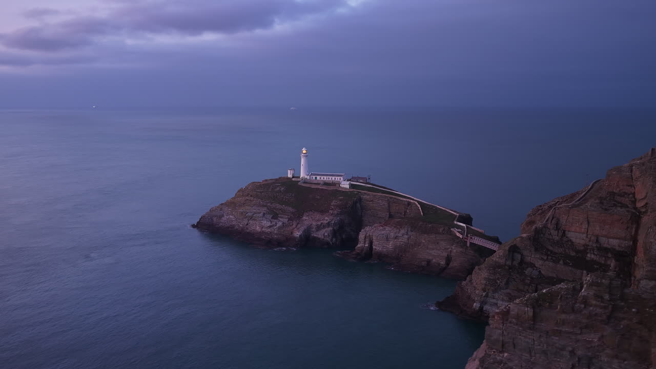 Riprese aeree con drone del Faro di South Stack sulla aspra costa gallese, scogliere drammatiche e onde atlantiche, un paesaggio marino cinematografico ideale per viaggi, natura, turismo costiero e uso documentaristico.