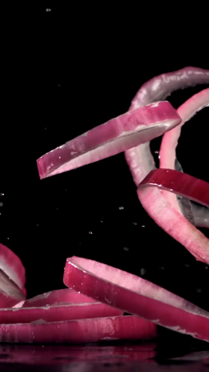 Vibrant Red Onion Rings Falling onto a Wet Surface in Slow Motion