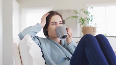 happy caucasian woman sitting on couch and drinking coffee