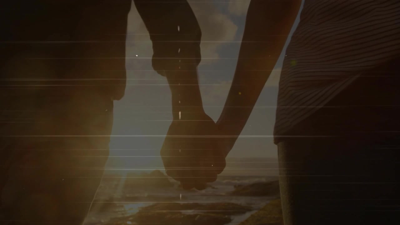 Couple stepping onto coast at sunset, interlocking fingers sharing connection with drifting flares