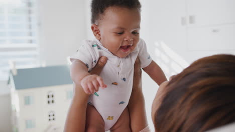 proud grandmother cuddling and playing with baby grandson in nursery at home