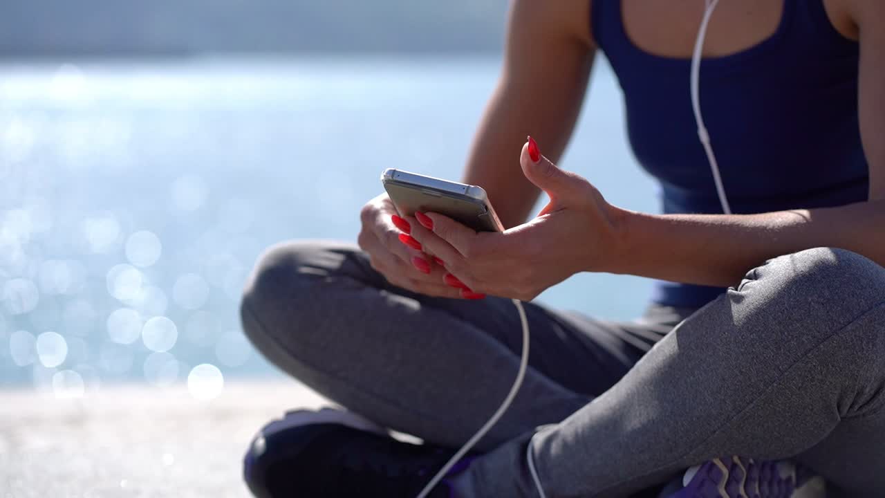 mujer joven deportiva con auriculares usando teléfono móvil al aire libre
