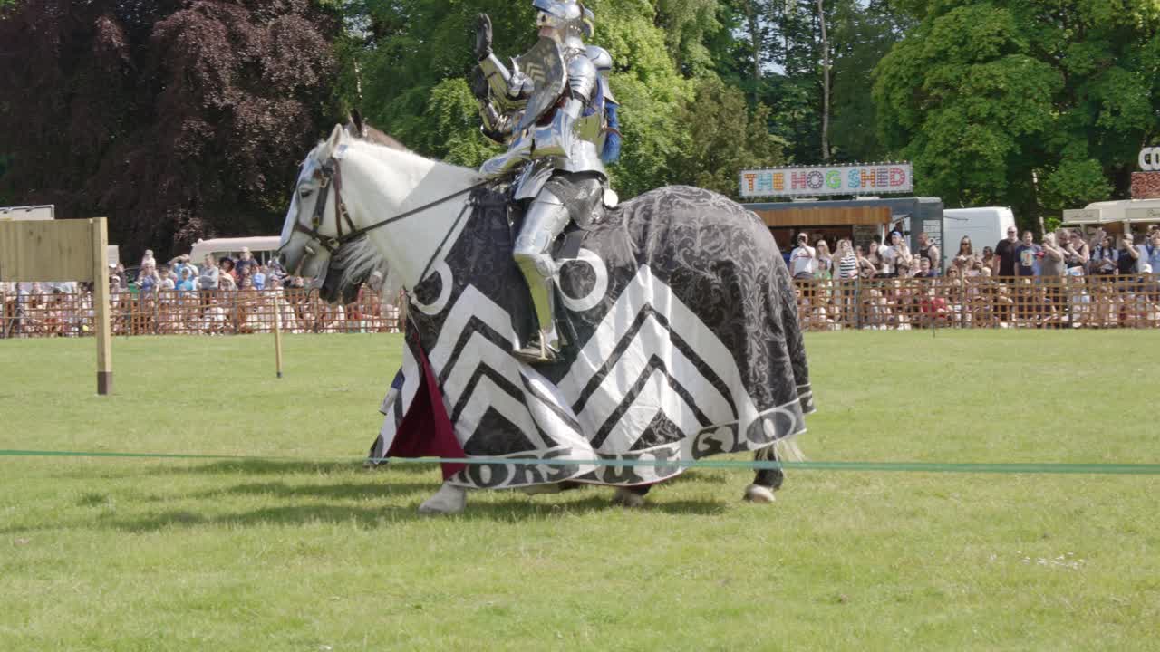 Armoured knights riding their horses wave as they enter the arena during a medieval tournament Joust at Leeds Castle, Kent, England