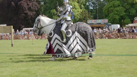 armoured knights riding their horses wave as they enter the arena during a medieval tournament joust at leeds castle, kent, england