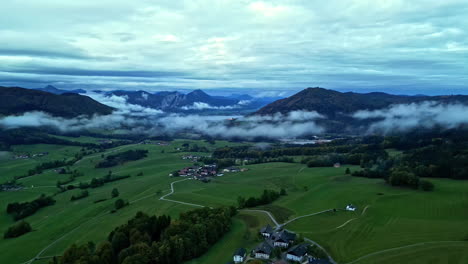 aerial isolated village in hills, early morning fog in open green valley, mountainous area