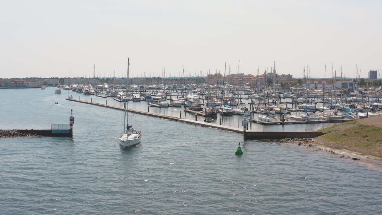 drone cinemático - toma aérea de un barco navegando en el océano con un puerto deportivo en el fondo con veleros en un día soleado en zelanda en el mar del norte, países bajos, 25p