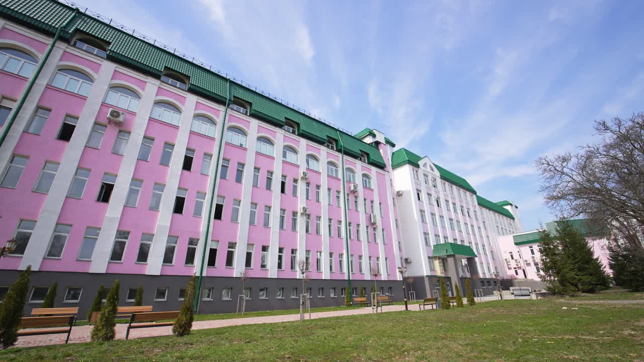 Beautiful pink and white building with green roof. Huge construction with lots of windows and without balconies. Low angle view.