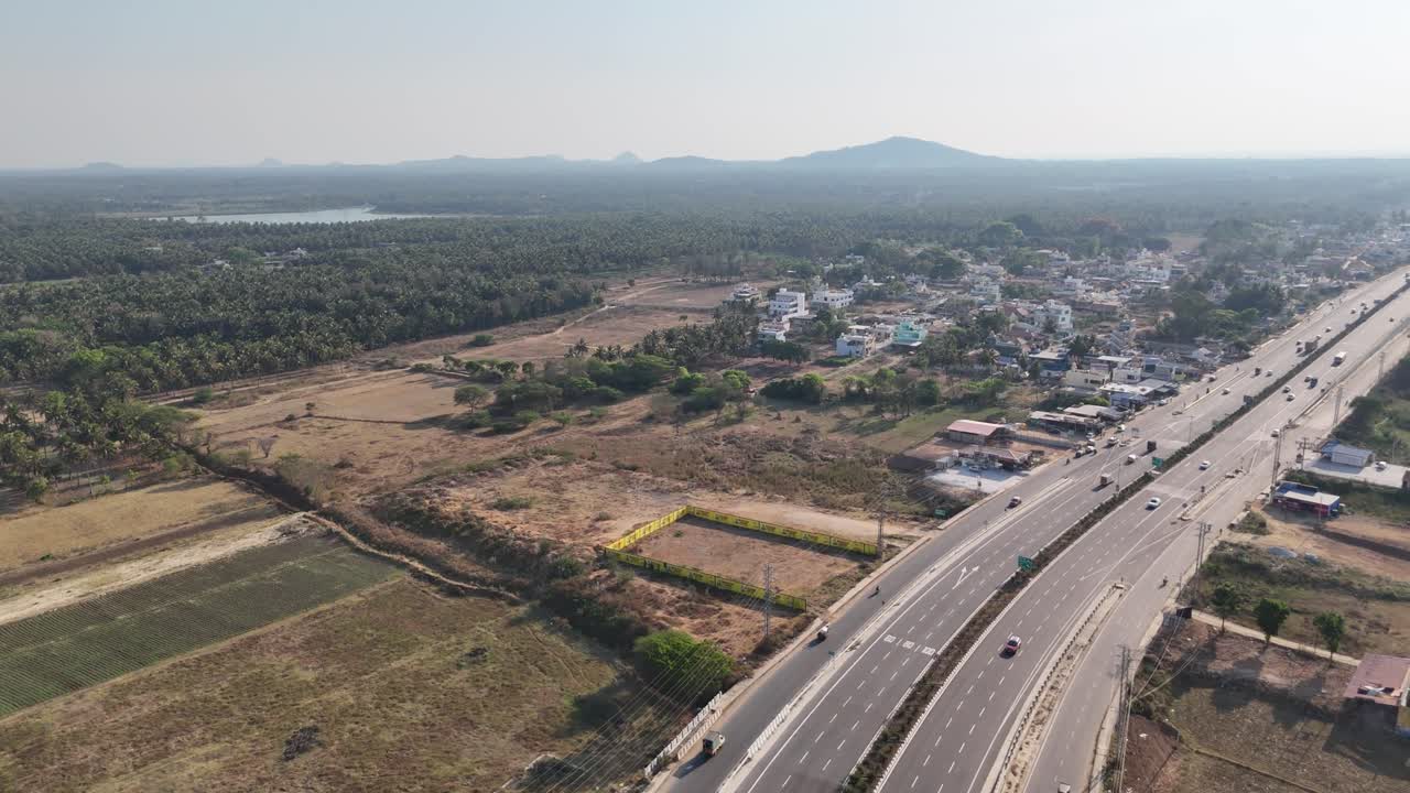 Expansive aerial footage: newly built highway in Karnataka. It winds past active farmlands, a lake, and distant mountains. Great for themes of progress, connectivity, and rural development