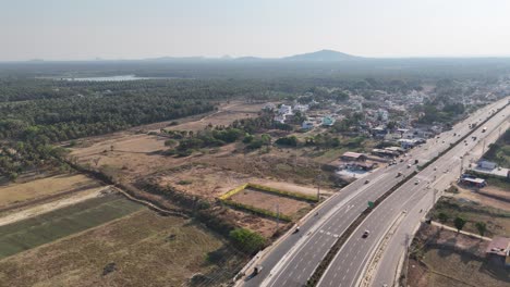 expansive aerial footage: newly built highway in karnataka. it winds past active farmlands, a lake, and distant mountains. great for themes of progress, connectivity, and rural development