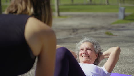 Smiling-senior-woman-preparing-to-do-abdominal-crunches-in-park.