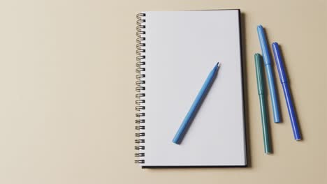 overhead view of notebook with blue markers on beige background, in slow motion