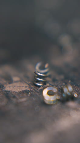 cu: goldsmith takes little metal link from rustic wooden table with thin pliers on blurred background extreme closeup