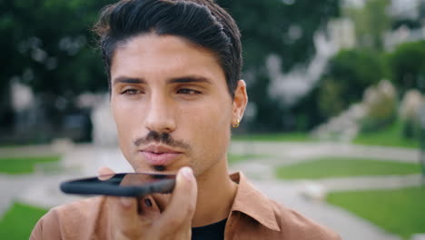 serious guy talking phone at parkland closeup. hispanic man recording message