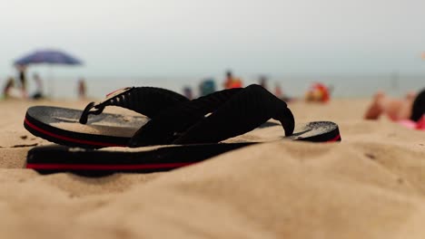 pair of black sandals covered in sand on a crowded beach