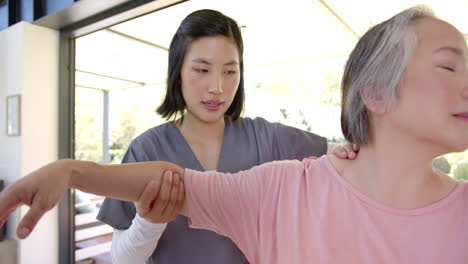 physiotherapist assisting senior asian woman with arm exercises at home therapy session