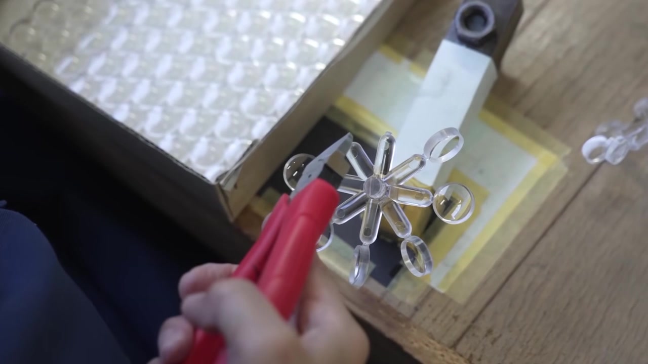 Worker trimming clear optical lens elements from injection mold sprue using red cutting pliers at factory workbench