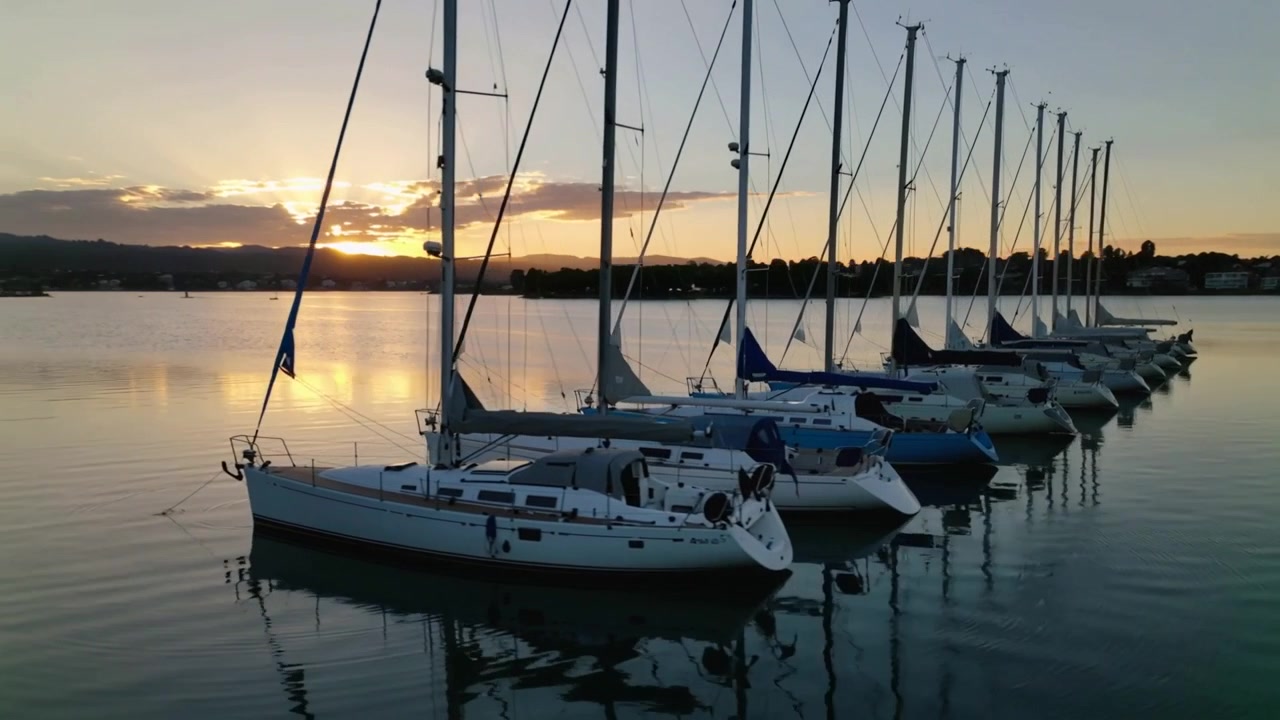 Caméra panoramique révélant une rangée unique de voiliers amarrés dans une marina, soulignant les reflets.