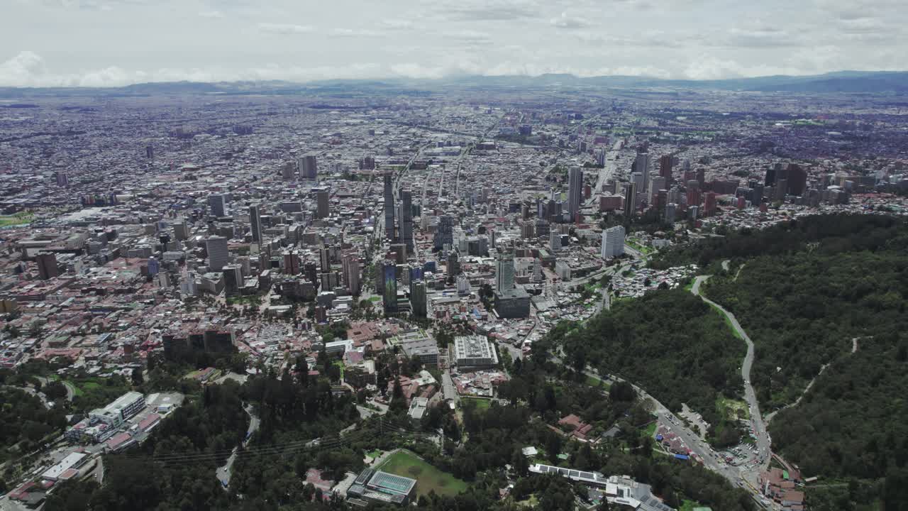 Aerial view of Bogota, Colombia, highlighting the dense urban landscape with modern buildings, residential areas, and the green slopes of Monserrate, framed by the Andres mountain ridge