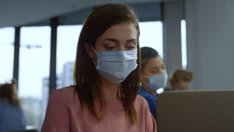 Focused-businesswoman-in-medical-mask-on-face-working-on-laptop-in-office