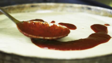 pizza sauce being spread onto thick pan pizza base