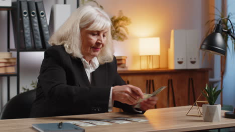 excited senior businesswoman counting cash money dollar checking salary enjoy richness at workplace
