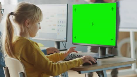 aula de ciencias de la computación de la escuela primaria: una niña linda usa una computadora de pantalla verde mientras aprende a codificar y programar. escolares que reciben una educación moderna. por encima del hombro