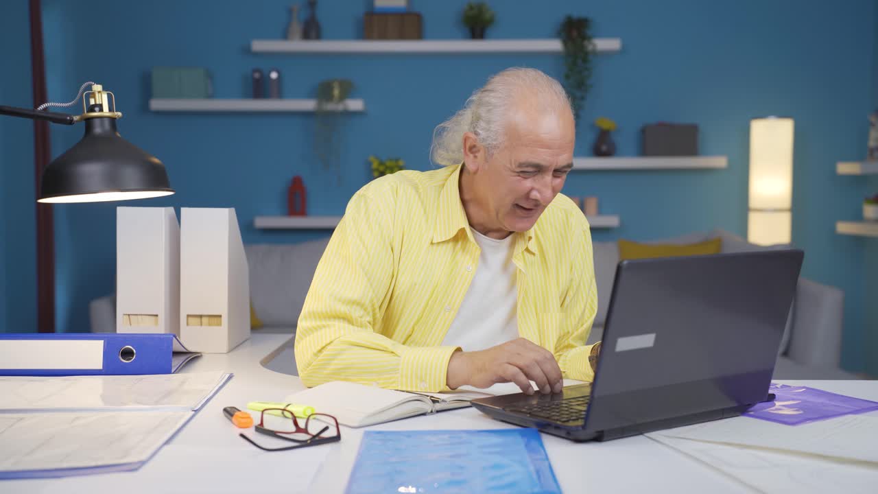 Home office worker old man rejoices at what he sees on the laptop.