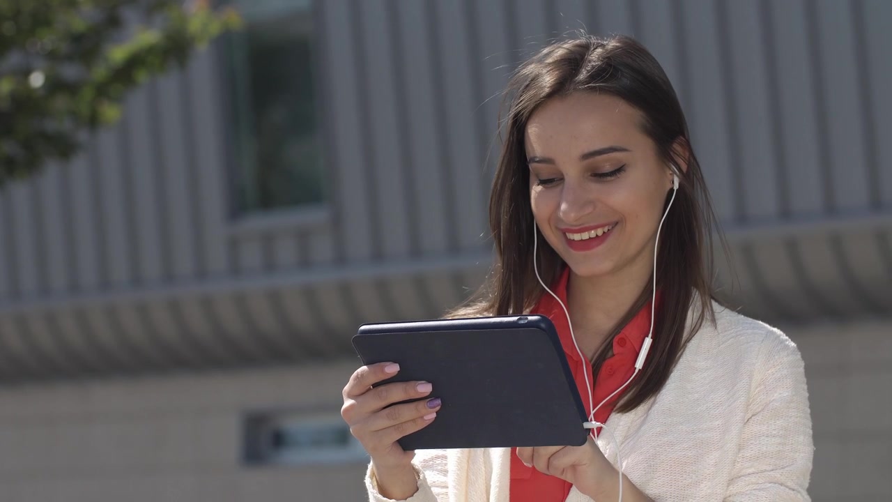 Happy Young Woman Using Tablet and Earphones Outdoors