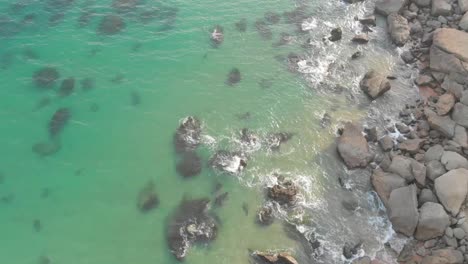 vista aérea sobre aguas poco profundas que chocan contra la costa rocosa en la playa de jiwani