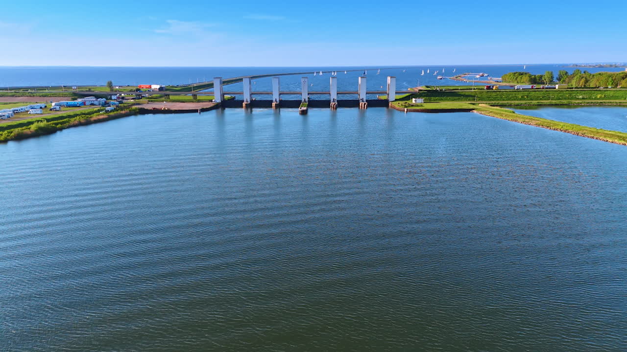 Gorgeous Dutch waterway view. A calm waterway reflects the clear sky, while boats sail in the distance near bridge pillars