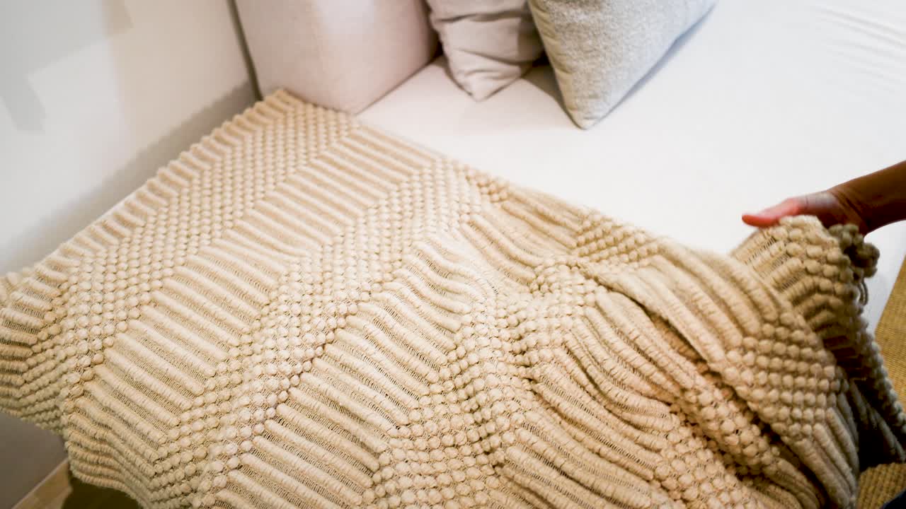 A person's hands carefully smooth and adjust a thick, textured beige woven rug indoors