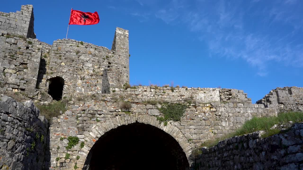 puerta arqueada del castillo albanés en shkodra con bandera ondeando en paredes de piedra