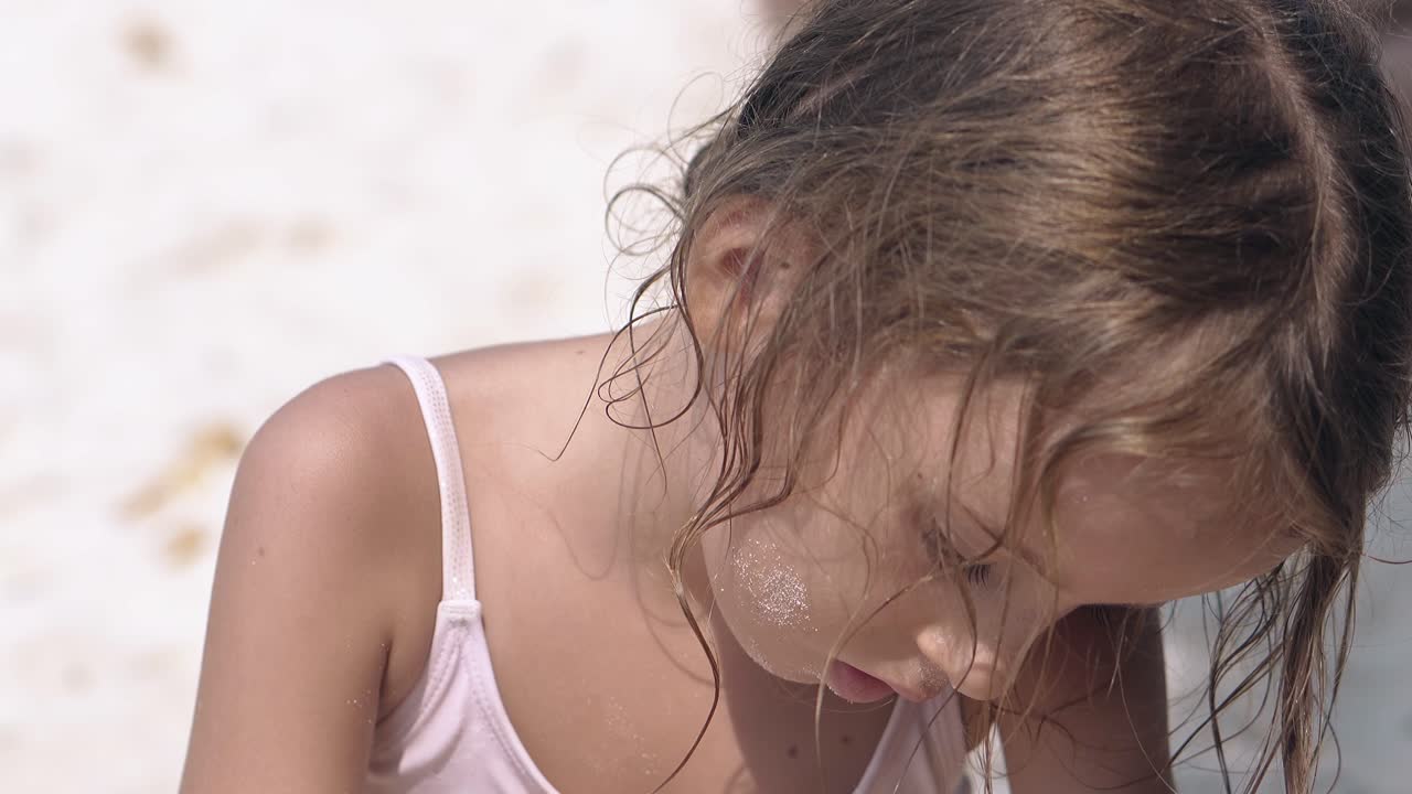 cerca una niña bonita de cabello claro se sienta en la playa y juega