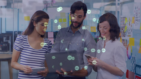 globo de iconos digitales contra diversos colegas de oficina masculinos y femeninos que usan computadoras portátiles en la oficina