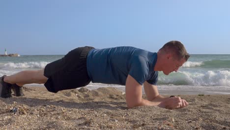 a young caucasian man with short hair doing push-ups on the sand beach by the sea with his connected watch