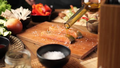 a young man pours oil over a piece of salmon surrounded by vegetables