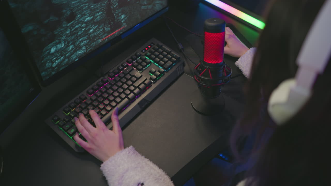 focused woman in fluffy sweater using colorful mechanical keyboard and mouse to play video game on screen with red microphone nearby inside vibrant gaming studio with LED lighting and tech setup
