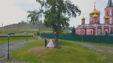 la novia y el novio bailan cerca del árbol contra la iglesia vista aérea