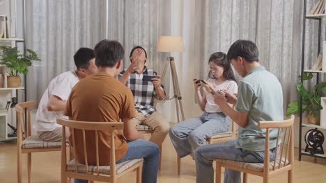 아시안 십대 그룹은 의자에 앉아서 집에서 스마트폰으로 게임을 하는 원을 형성합니다.