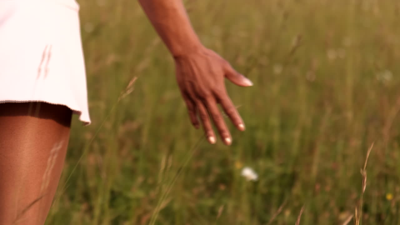 Black woman walks through the meadows in high grass touching the flowers and big bluestem