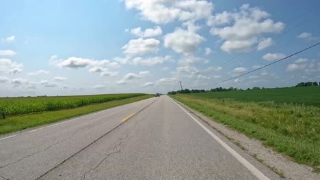 pov - driving on a rural county road past soybean fields and corn fields in late summer in central iowa