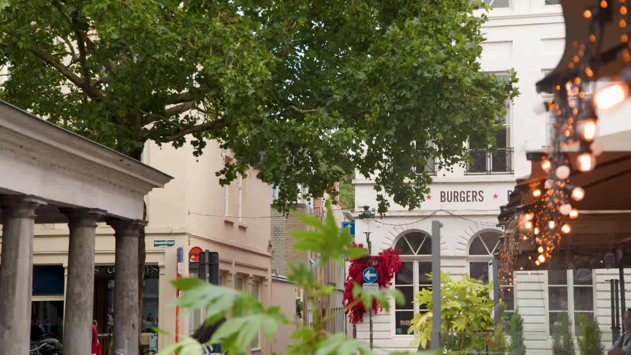 Cozy Bruges alley with outdoor cafe, festoon lights, lush trees, gentle camera movement, evening ambiance
