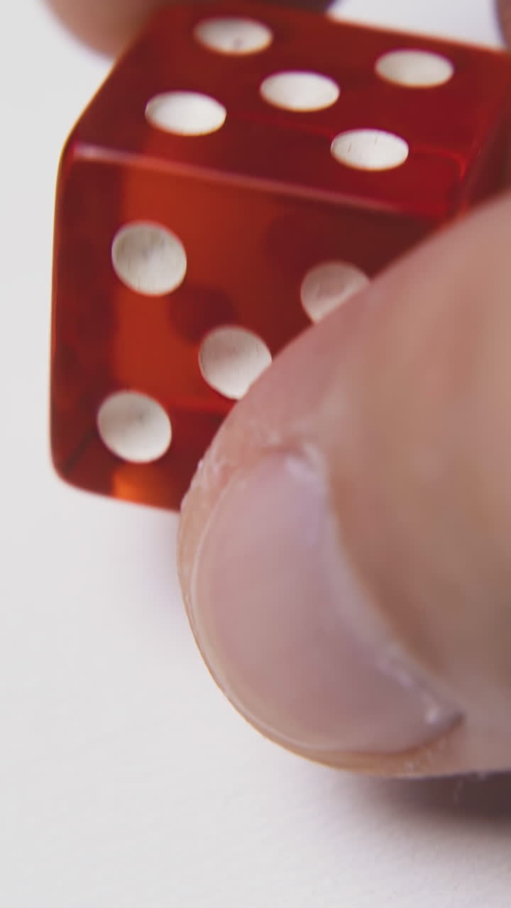 young person plays with red transparent plastic dices with white spots on light background extreme close view