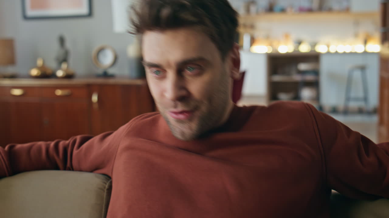 Smiling guy looking mobile phone screen on couch closeup. Man reading message
