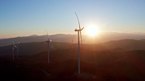 turbinas eólicas em silhueta em uma paisagem montanhosa com o sol cobrindo o horizonte em uma vista aérea serena