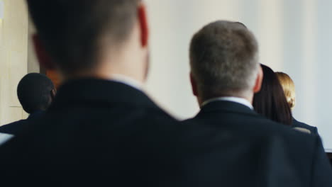 rear view of people sitting in a conference room who are listening to a caucasian businessman talking on a podium