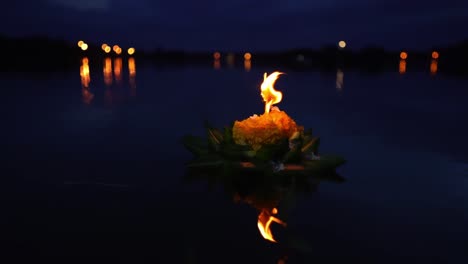 Loy-Krathong-Festival:-Wunderschöner-Krathong-Aus-Bananenblättern-Und-Orangefarbenen-Blüten-Mit-Einer-Brennenden-Kerzenspitze-Auf-Dem-Dunkelblauen-Wasser