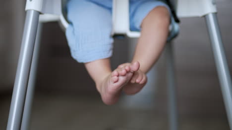 cute little baby feet. small child sitting at the feeding chair moves his legs cheerfully. close up. blurred backdrop.
